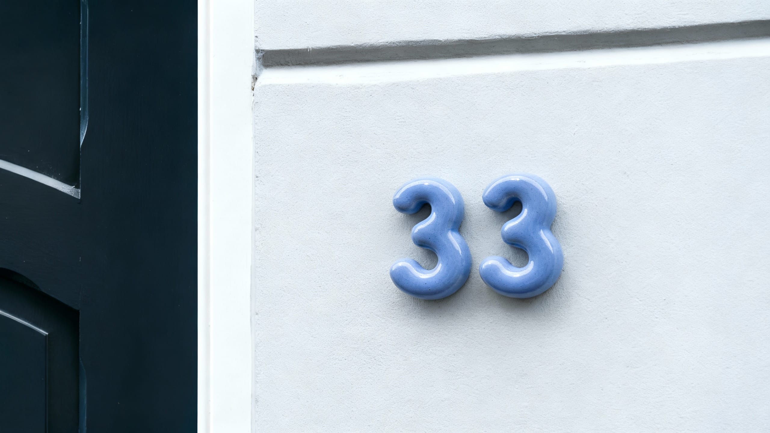 Blue house ceramic numbers '33' on a white door