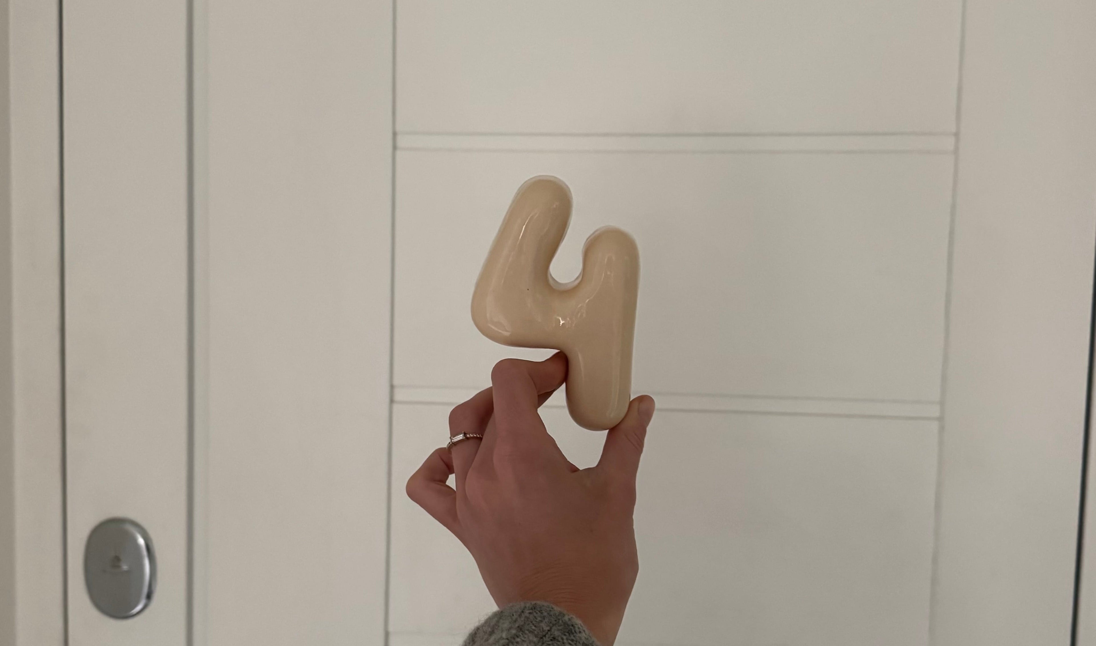 Hand holding a clay beige number '4' against a white wall
