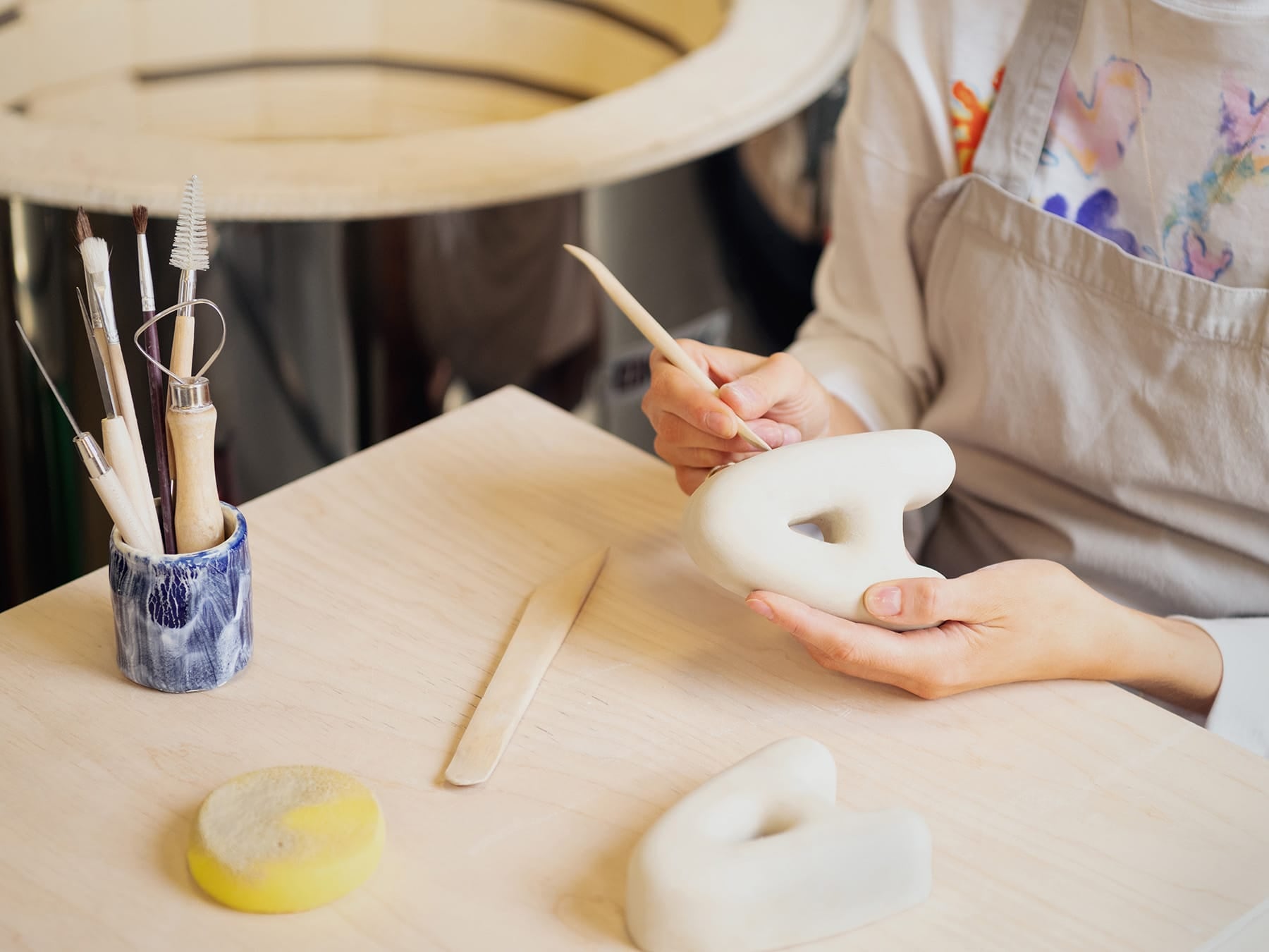 A person working with ceramic letters on a table, wearing an apron.