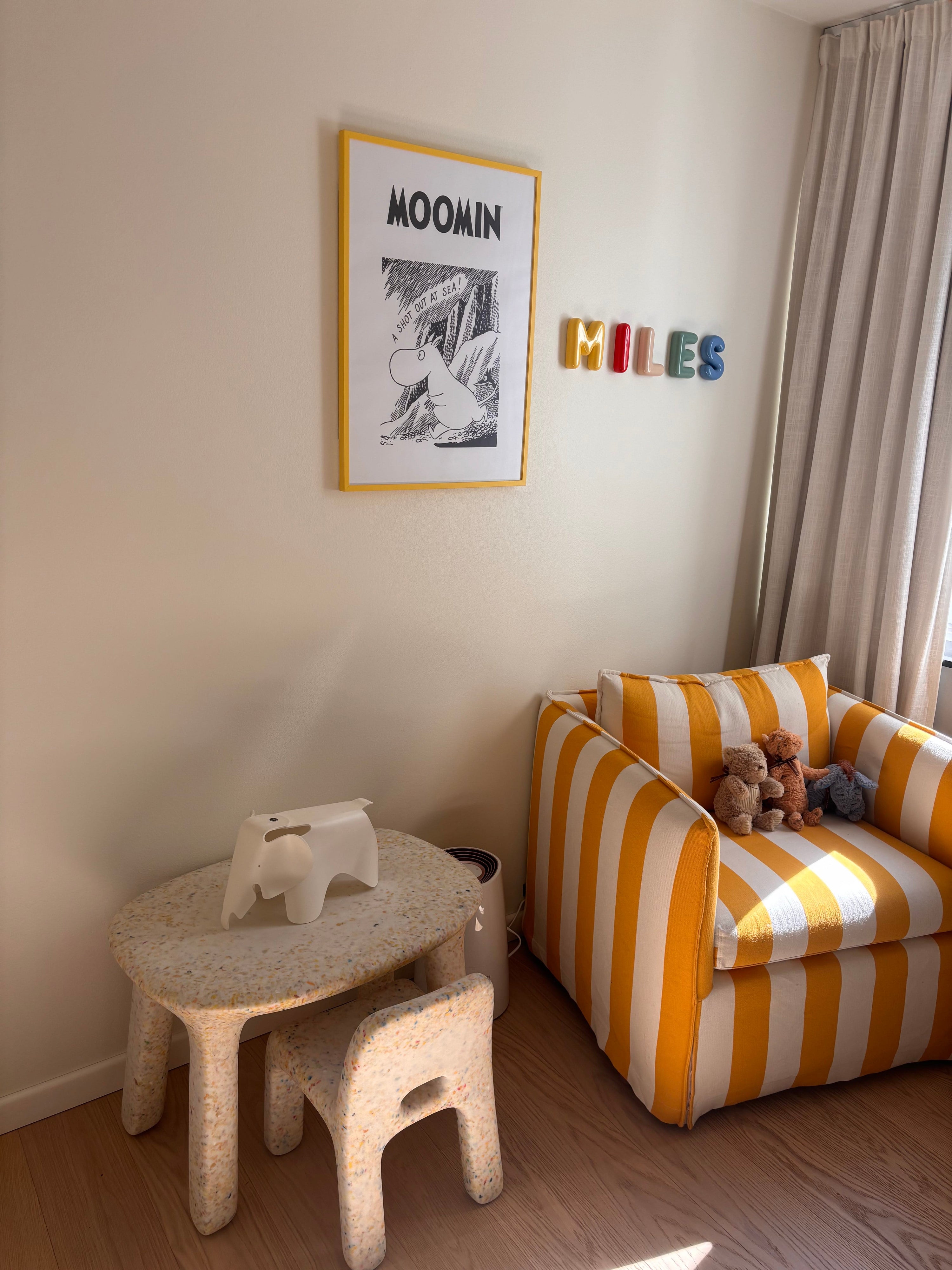 Colourful ceramic name letters spelling MILES mounted on a child's playroom wall above a striped armchair, a personalized children's gift that moves beyond the nursery