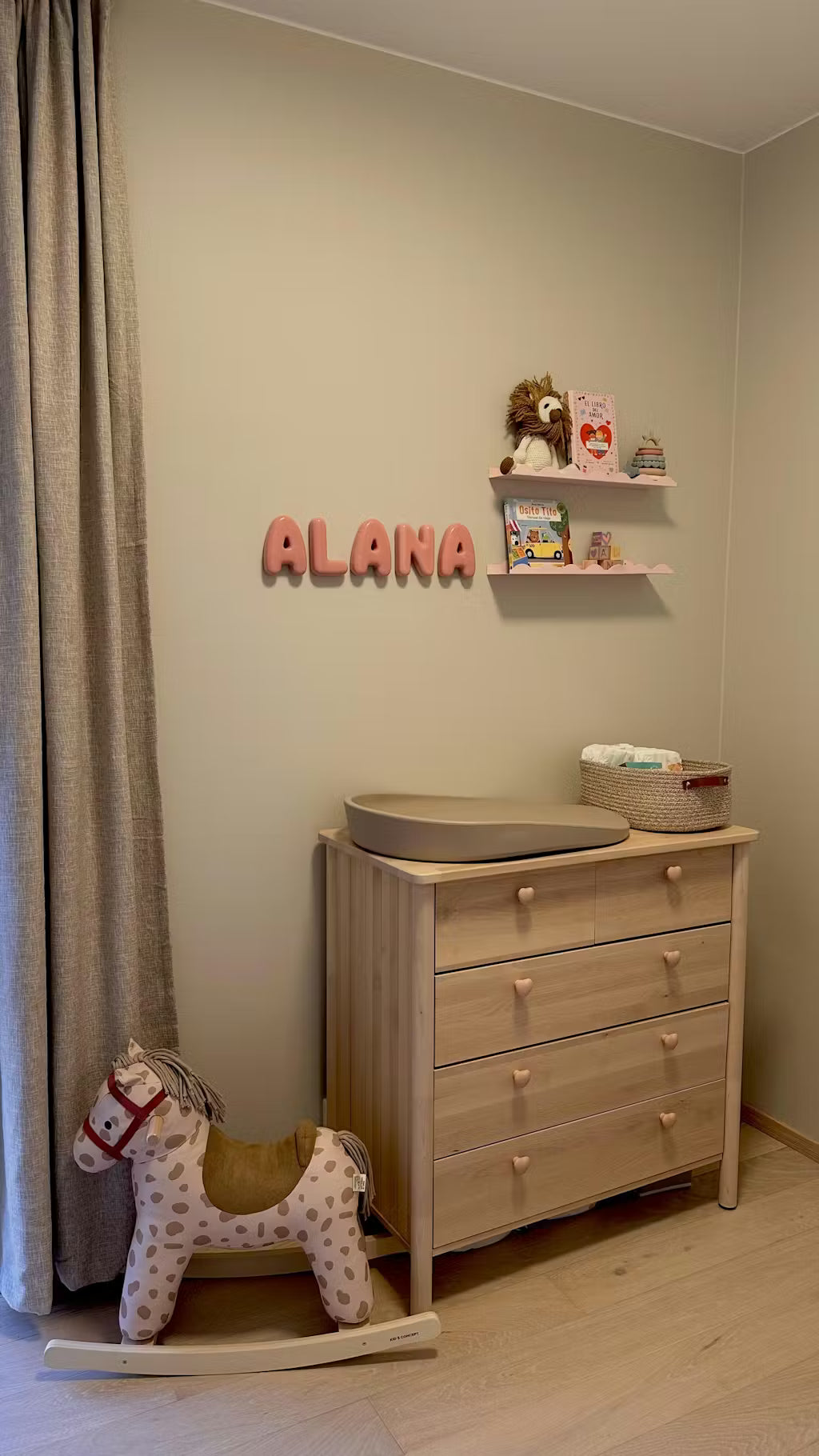 Nursery room with wooden changing table, rocking horse, and 'ALANA' wall decor.