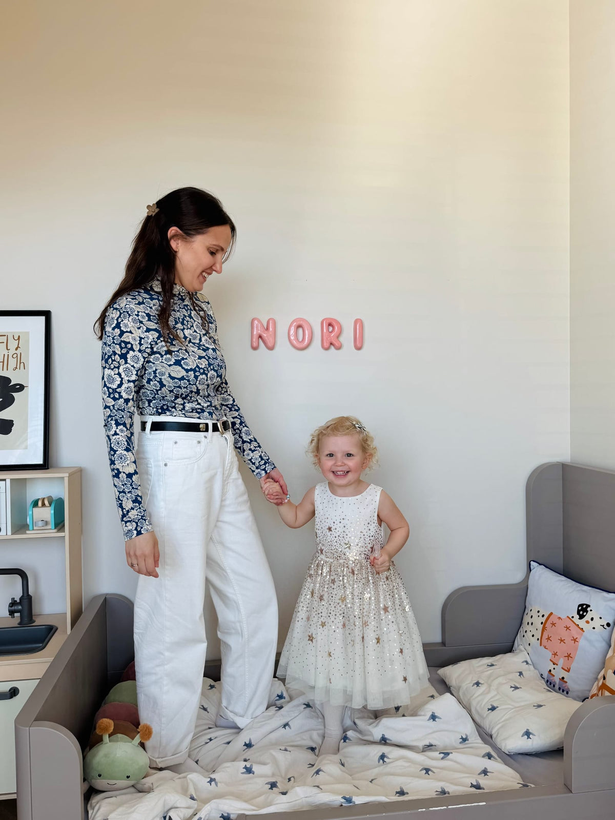 A woman and a child standing in a nursery room with ceramic letters 'Nori' on the wall