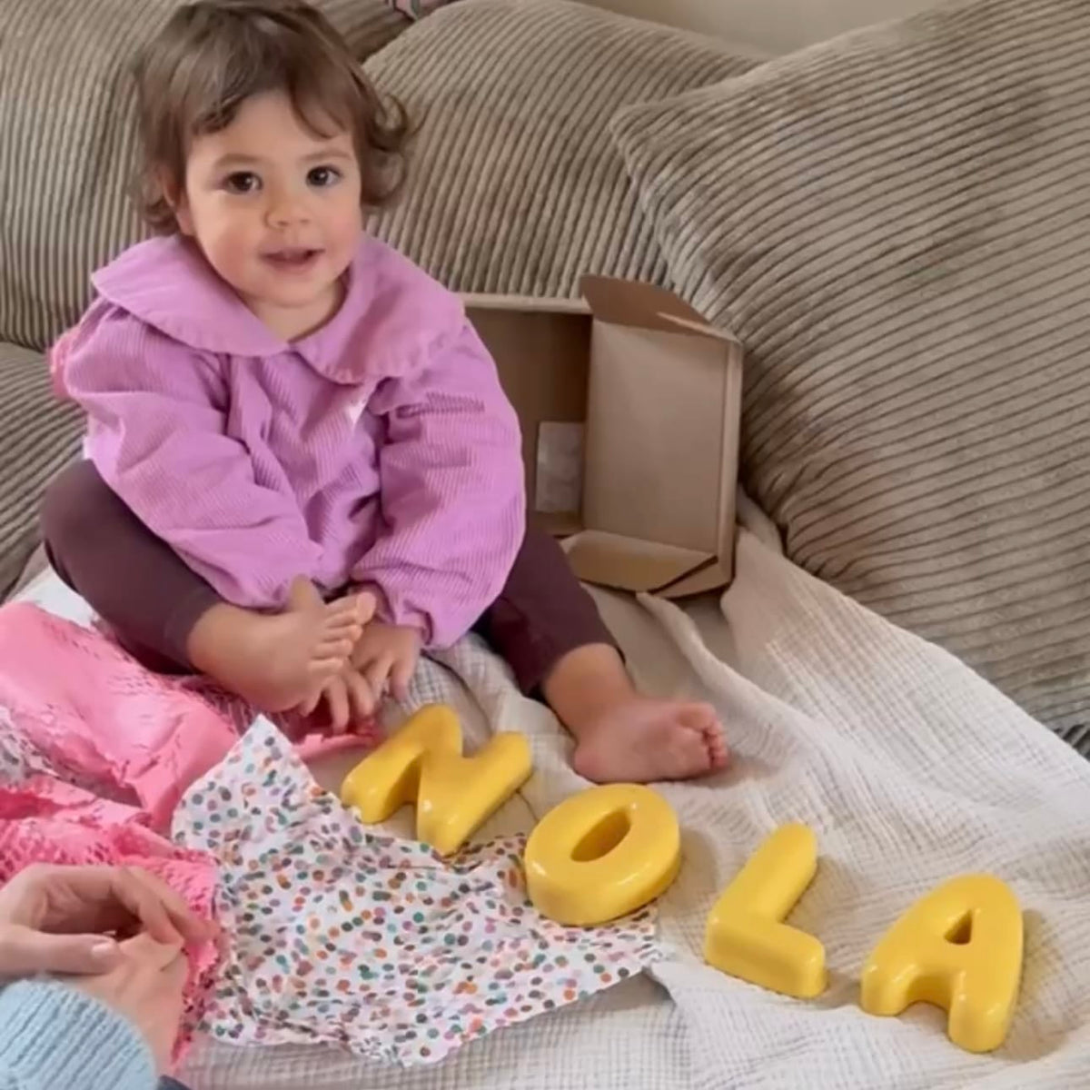 Child sitting on a couch with yellow clay letters spelling 'NOLA' in front of them.