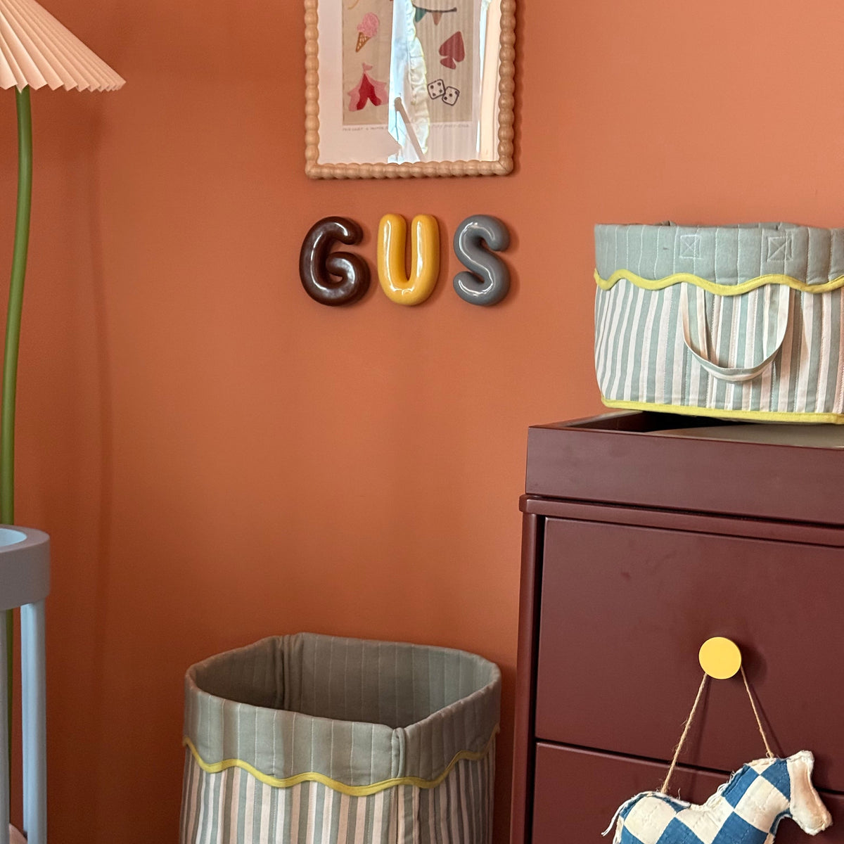 Children's room with orange wall, 'GUS' letters, dresser, and toy horse.