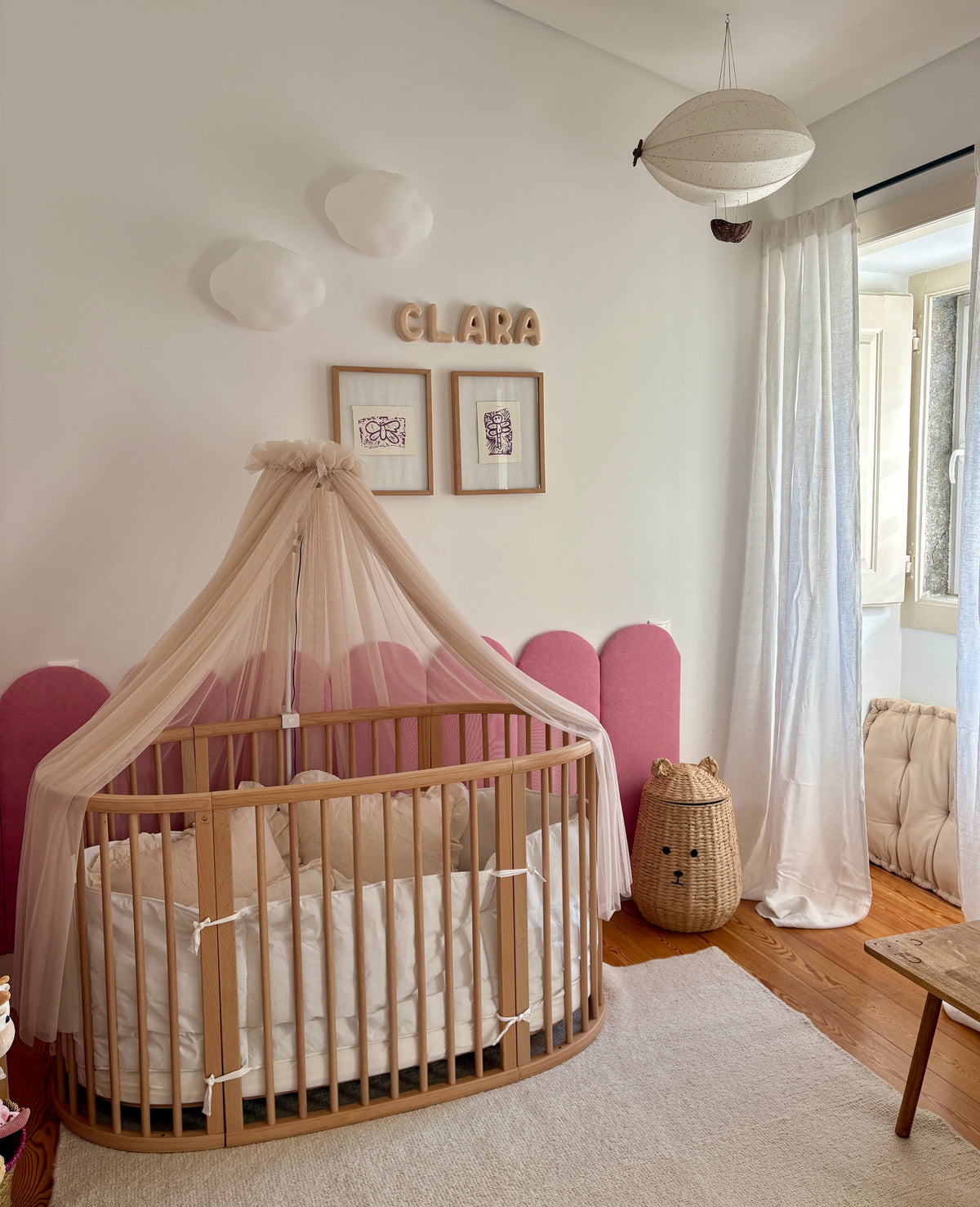 Nursery room with wooden crib, pink headboard, and decorative elements.